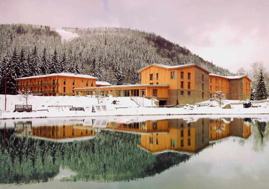 um edifício na neve ao lado de um corpo de água em Apartmán Medvědín 110 em Spindleruv Mlyn