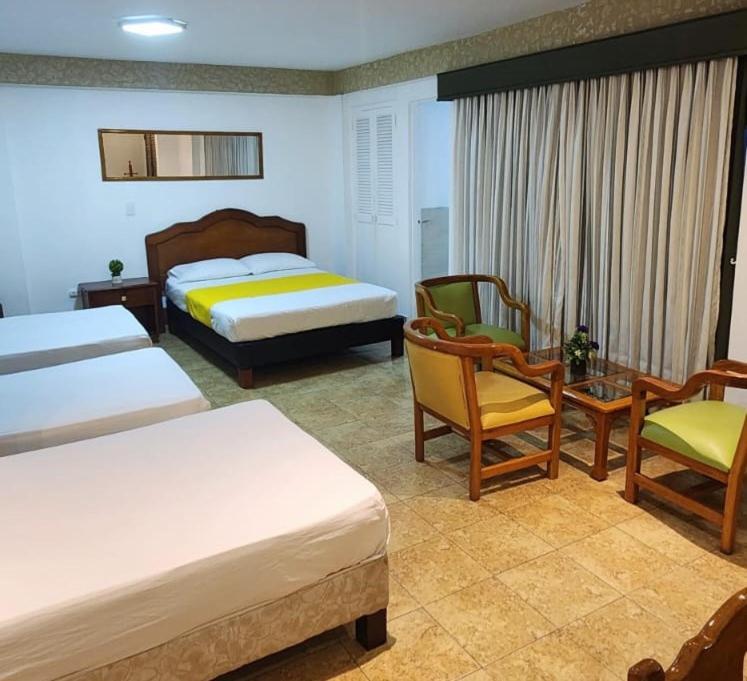 a bedroom with two beds and chairs and a table at Hotel Laureles 70 in Medellín