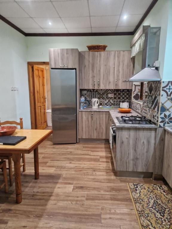 cocina con armarios de madera, mesa y nevera en Sir Patrick's rooms & hostel, en Għajn il-Kbira