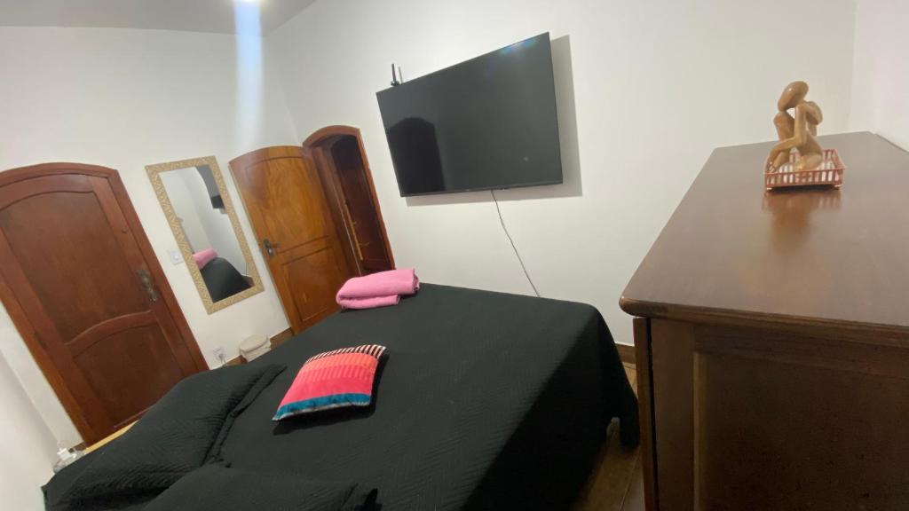 een slaapkamer met een bed met een zwarte deken en een tv bij Quarto aconchegante II in Cruzeiro
