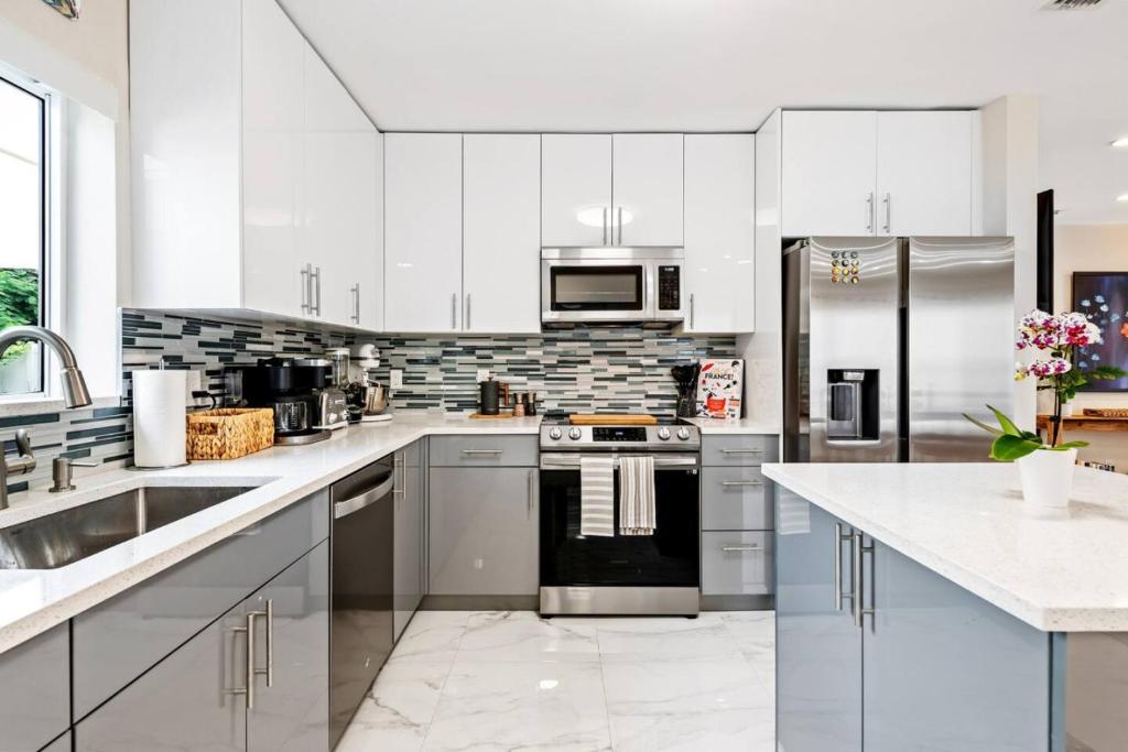 una cocina con armarios blancos y electrodomésticos de acero inoxidable en Modern Bungalow near Wilton Drive I Pool Table en Fort Lauderdale