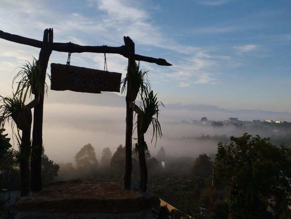 a sign hanging from a pole on a hill with a foggy valley at Homestay Chân Quê in Bao Loc