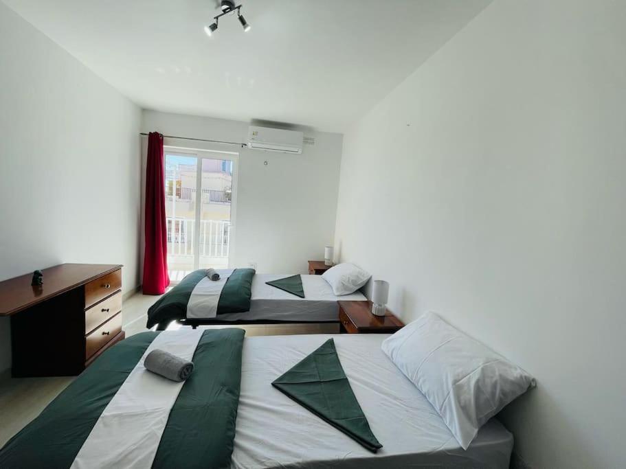 1 Schlafzimmer mit 2 Betten, einem Schreibtisch und einem Fenster in der Unterkunft Coral Cove Comfort Apartment Room 3 in St Paul's Bay