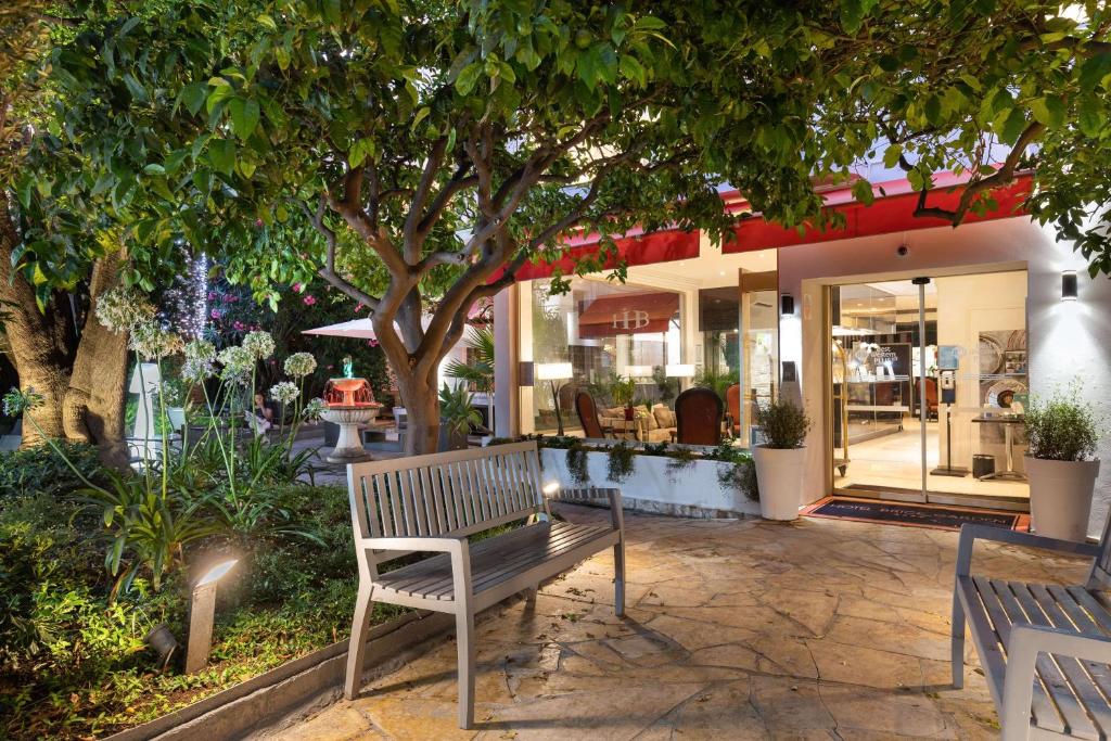 a bench sitting under a tree in front of a store at Best Western Plus Hôtel Brice Garden Nice in Nice