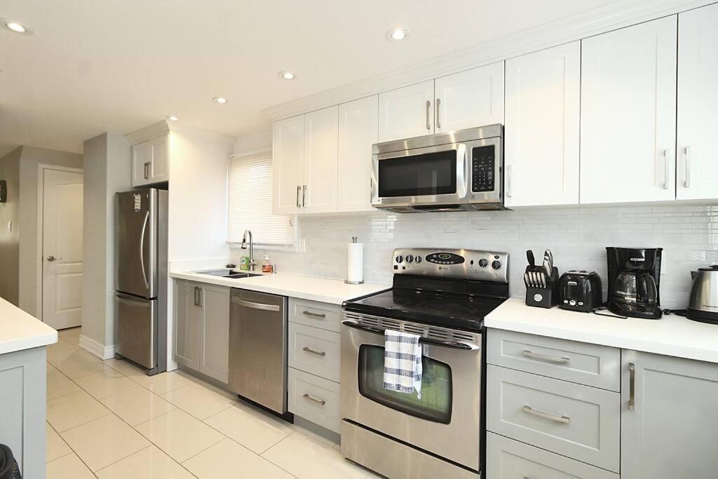 una cucina con elettrodomestici in acciaio inossidabile e armadietti bianchi di Barrie House near to all amenities a Barrie