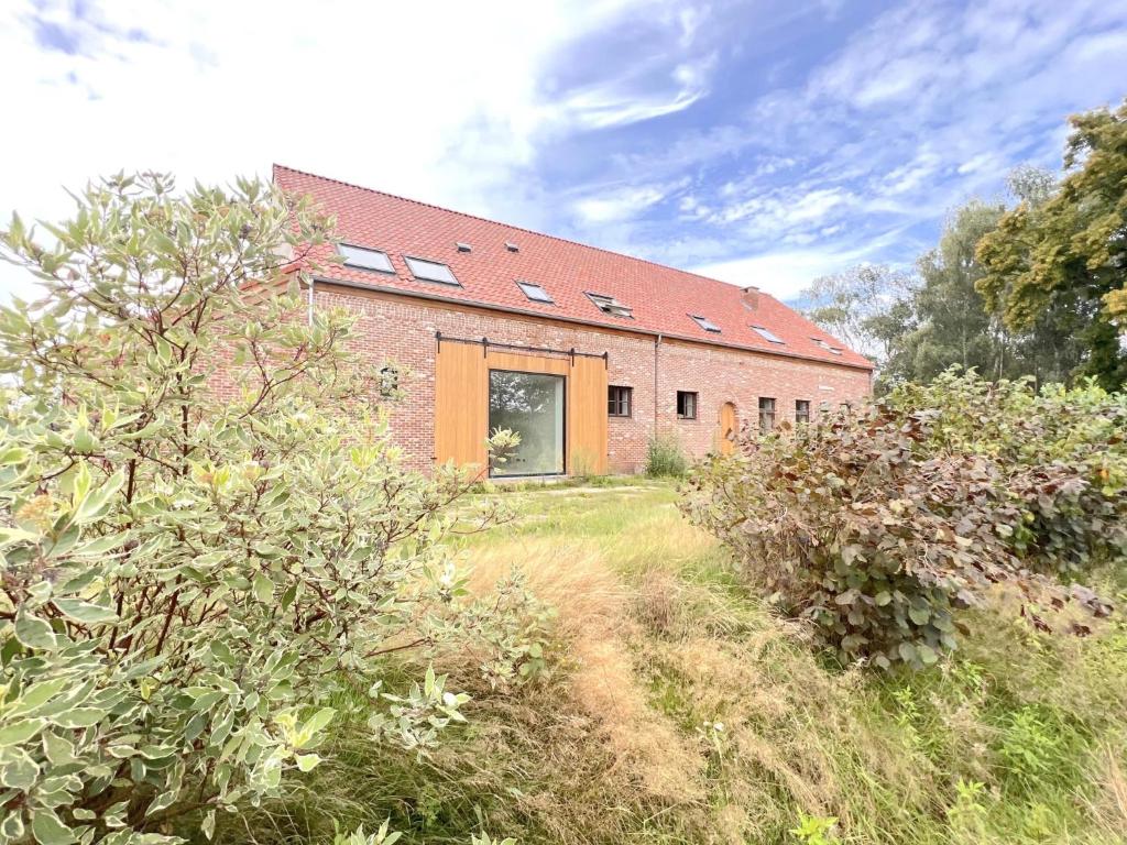 un bâtiment en briques avec une grande fenêtre dans un champ dans l'établissement Lindehoeve, à Turnhout