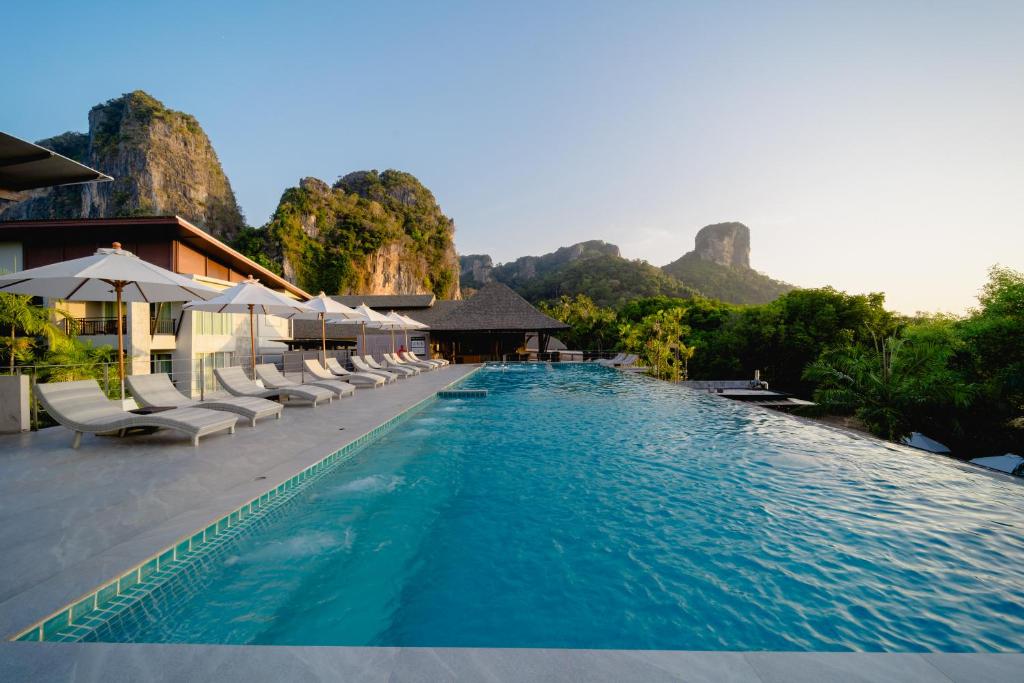 a swimming pool with chairs and mountains in the background at Railay Princess Resort & Spa-SHA Extra Plus in Railay Beach