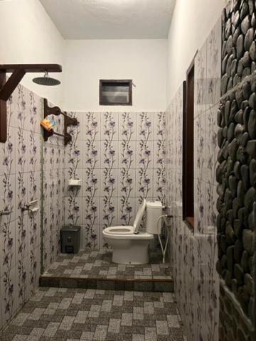 a bathroom with a toilet and a tiled wall at R5 Keramba Inn in Bukit Lawang