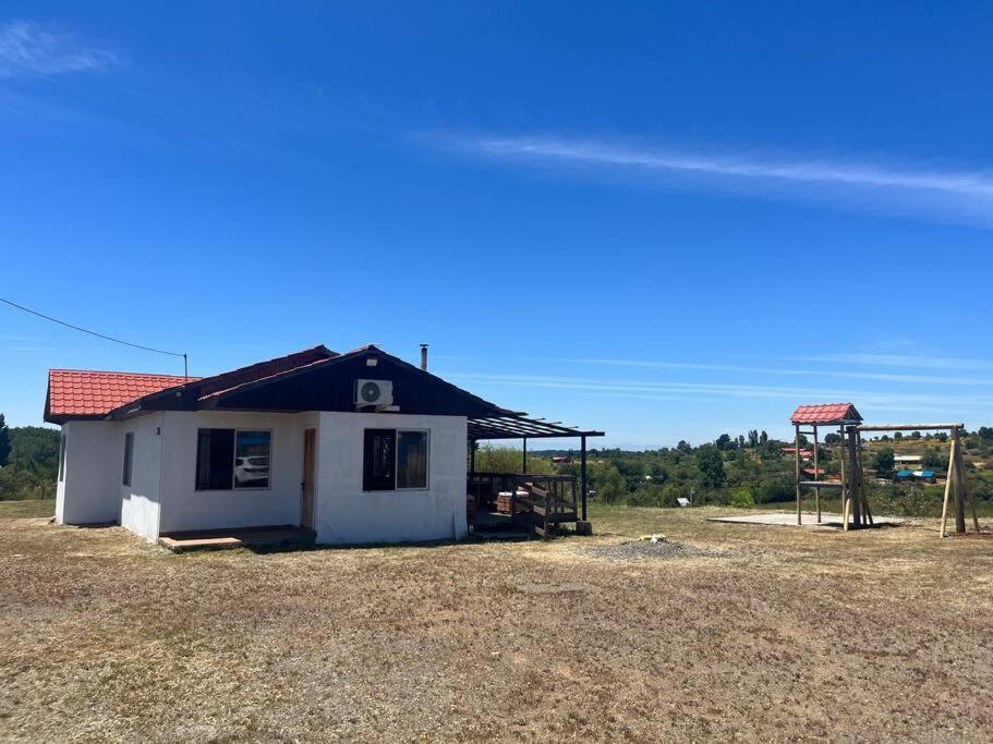 una pequeña casa blanca con techo rojo en un campo en Casa los cabreras en Quillón