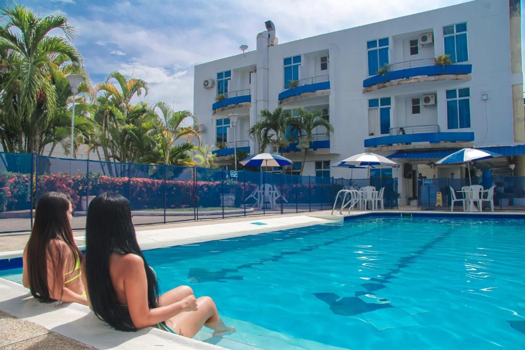 two women sitting next to a swimming pool at a hotel at Hotel Miami en Melgar in Melgar