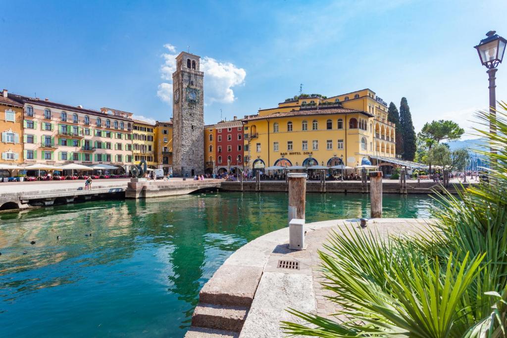 a river in a city with buildings and a clock tower at Hotel Sole Relax & Panorama in Riva del Garda