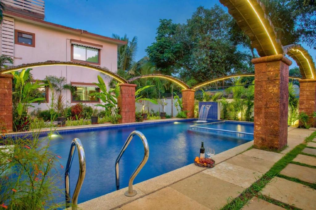 STAR HOLIDAY VILLAS في أنجونا: حمام سباحة مع زجاجة من النبيذ بجوار منزل