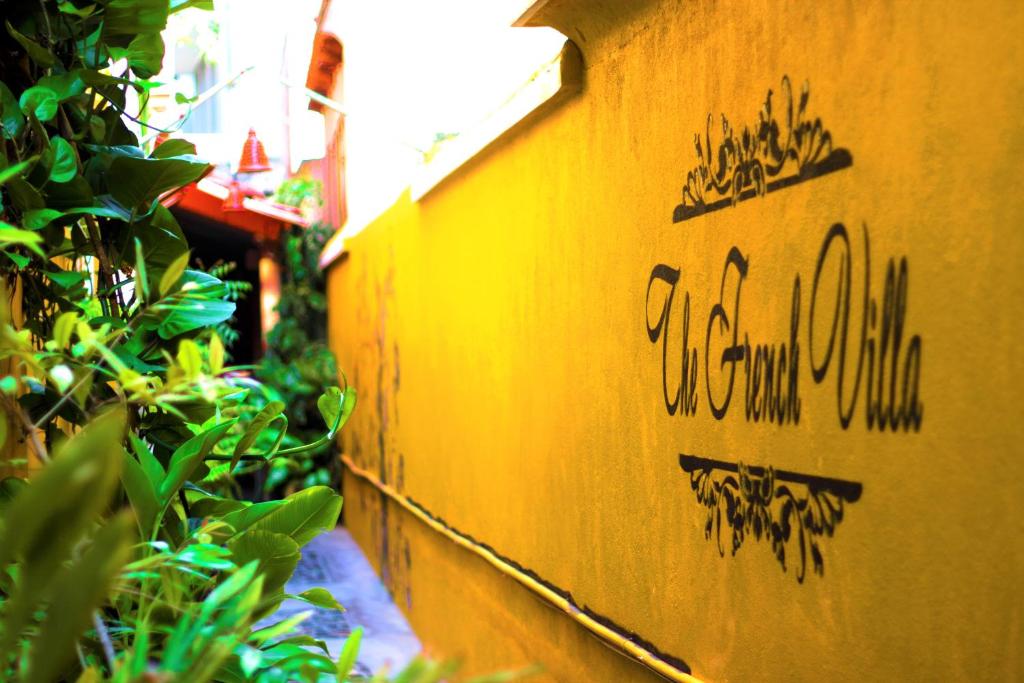 un mur jaune avec inscription à côté des plantes dans l'établissement The French Villa, à Pondichéry