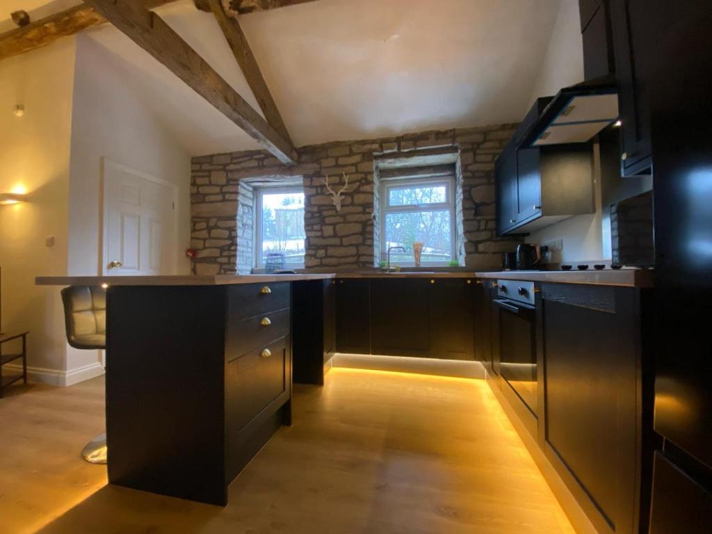 a kitchen with black cabinets and a stone wall at Robins mill in Rishworth