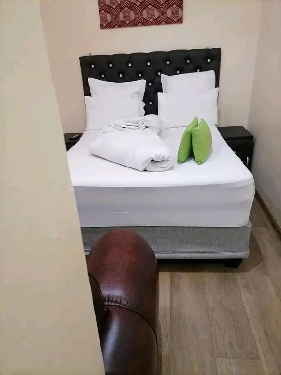 Una cama blanca con dos almohadas verdes. en Rizhatchguest, en Mahikeng