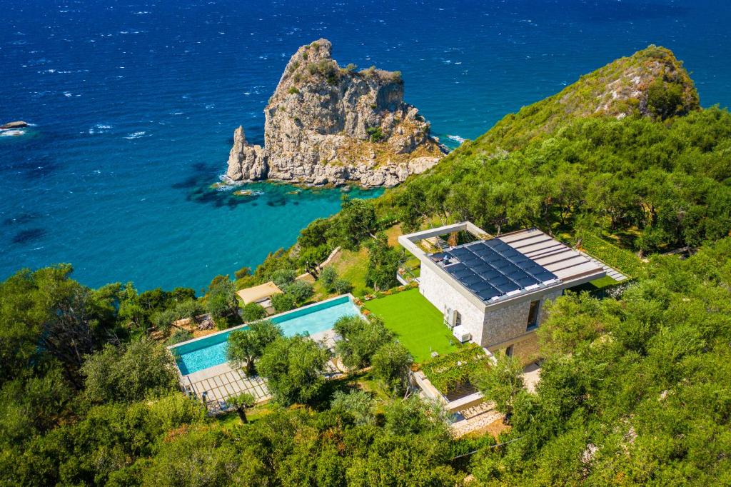 una casa con paneles solares en una colina junto al océano en Amberton Green Villas Corfu en Corfú