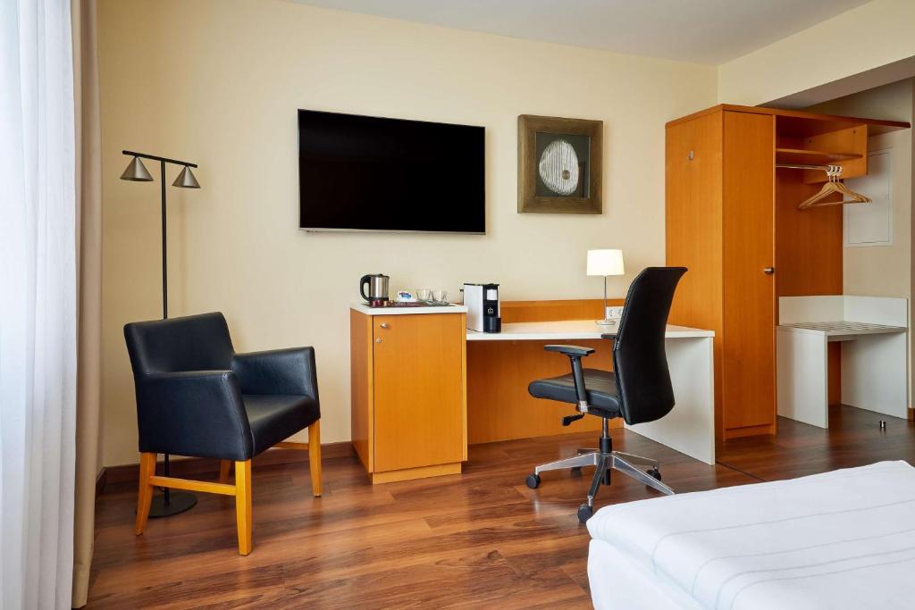 a room with a desk and two chairs and a tv at Best Western Macrander Hotel Dresden in Dresden