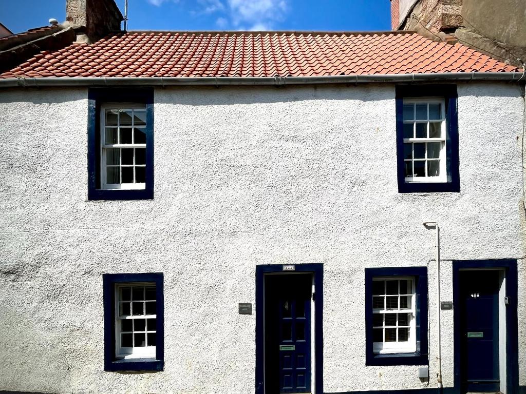 een wit huis met blauwe ramen en een rood dak bij Smugglers Neuk - cosy hideaway for 2 in Cellardyke in Cellardyke