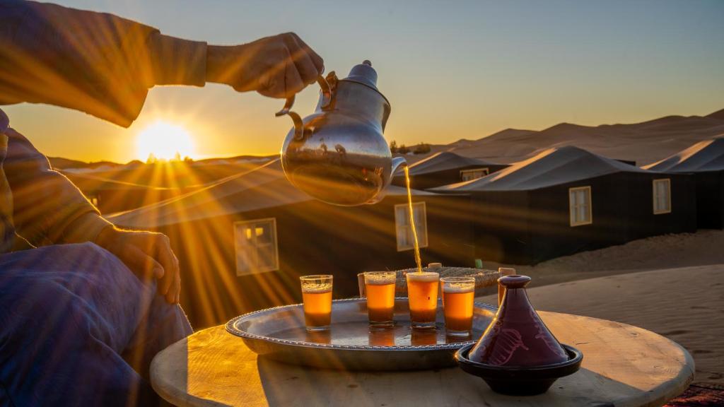 une personne versant du jus d'orange dans des verres sur une table dans l'établissement Nomad Camp, à Erfoud