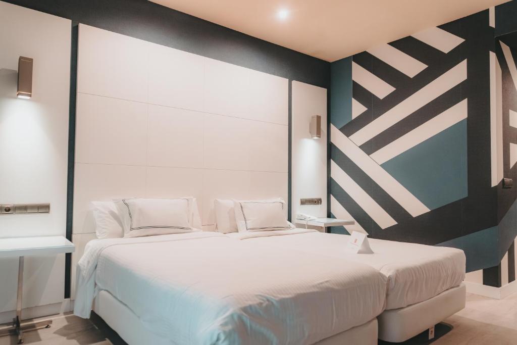 - une chambre avec un grand lit blanc et un mur dans l'établissement Hotel Málaga Nostrum Airport, à Malaga