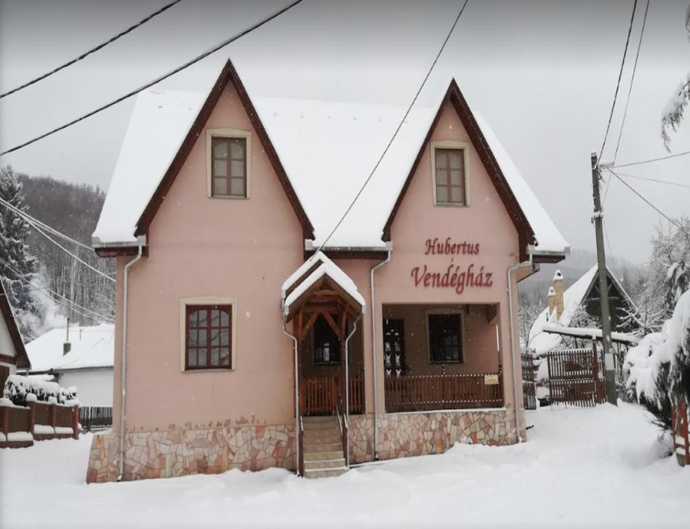 ein rosafarbenes Gebäude mit einem Schild im Schnee in der Unterkunft Hubertus Vendégház in Parád