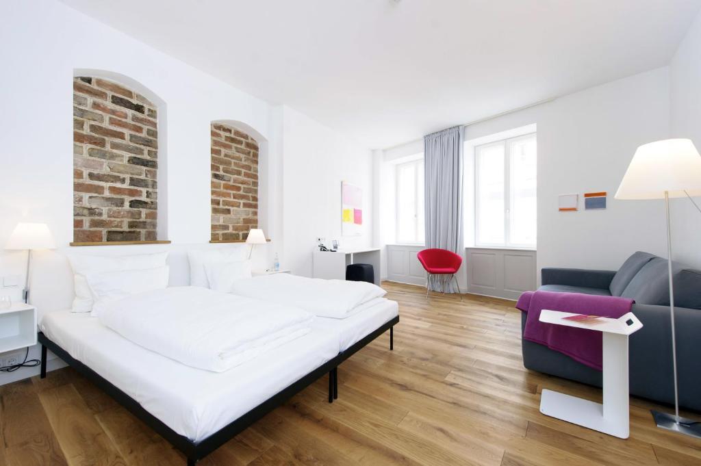 a white bedroom with a bed and a red chair at einzigartig - Das kleine Hotel im Wasserviertel in Lüneburg