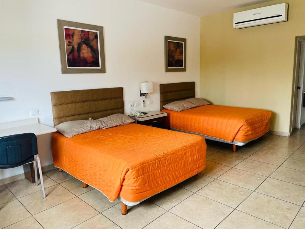 two beds in a hotel room with orange sheets at Hotel las Palmas in Hermosillo