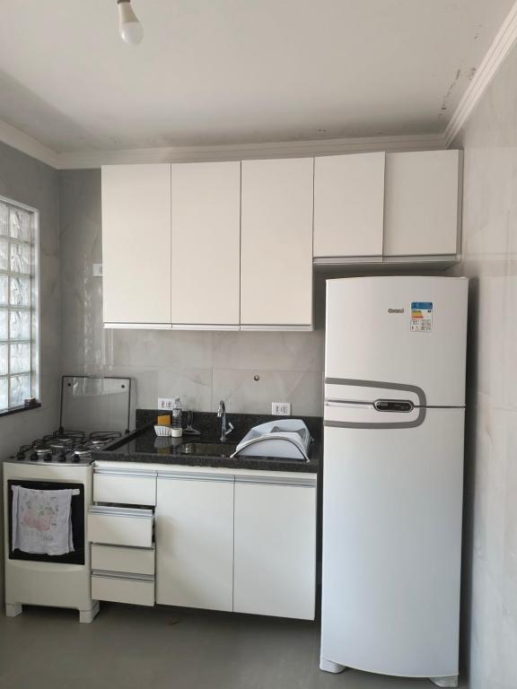 La cuisine est équipée de placards blancs et d'un réfrigérateur blanc. dans l'établissement Astúrias, à Guarujá