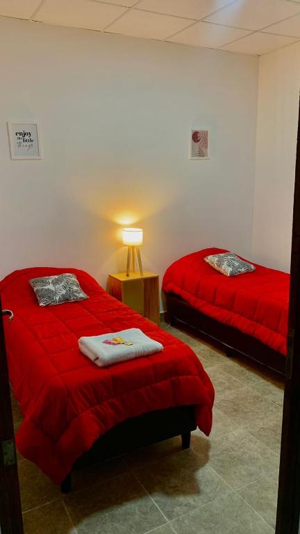 two beds in a room with red sheets and a lamp at La acequia casa in Cafayate
