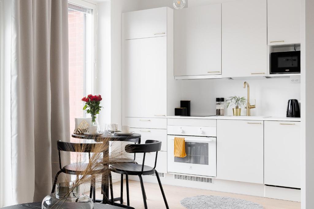 uma cozinha com armários brancos e uma mesa e cadeiras em Great location, quiet and new with balcony&cafe em Tampere