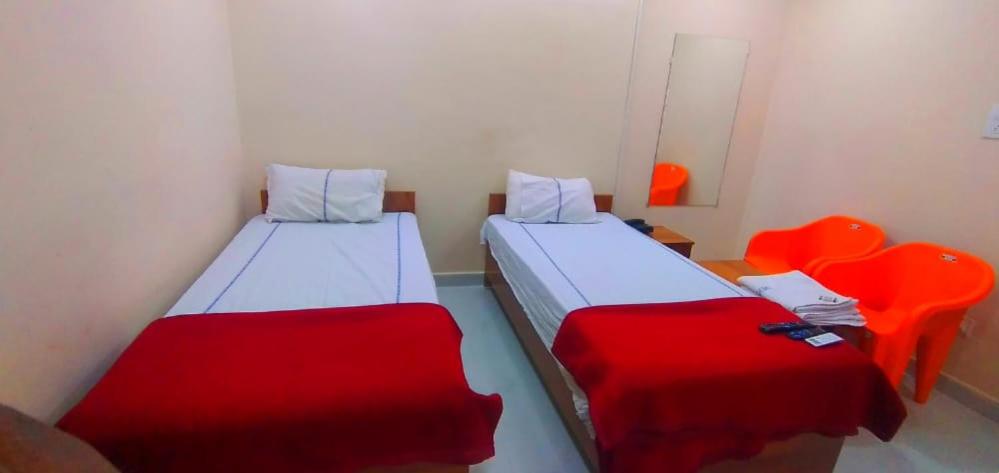 twee bedden in een kleine kamer met rode lakens bij SNEHA INN in Mancherāl