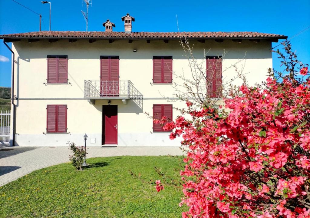 a white house with red shutters and a bush with pink flowers at Casa Laura in Magliano Alfieri