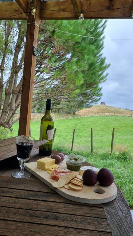 a table with a plate of cheese and a bottle of wine at Kereru Cottage in Whakamarama