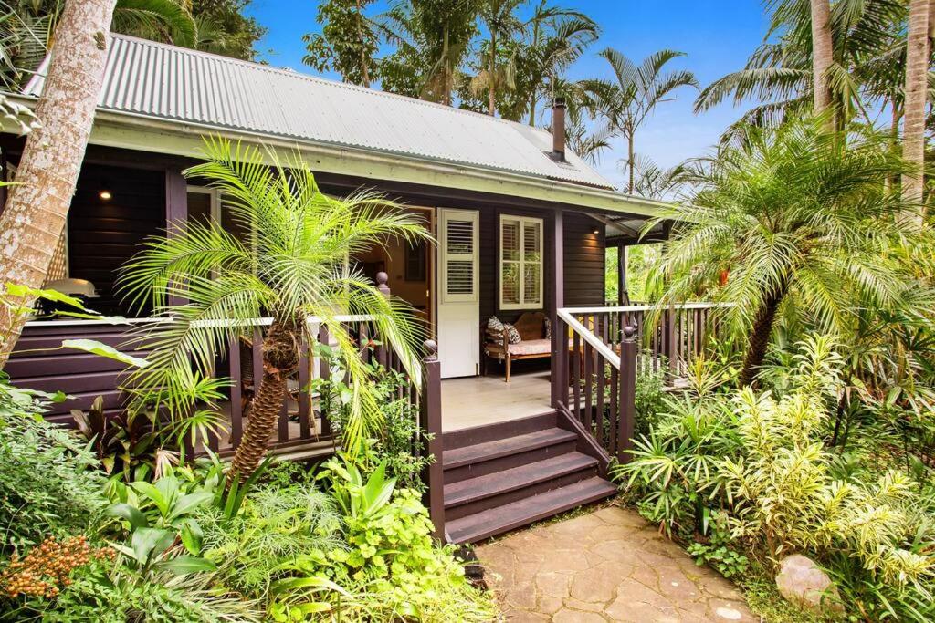 a small house with a wooden porch and palm trees at Coco's Cottage in the Byron Bay Hinterland in Bangalow