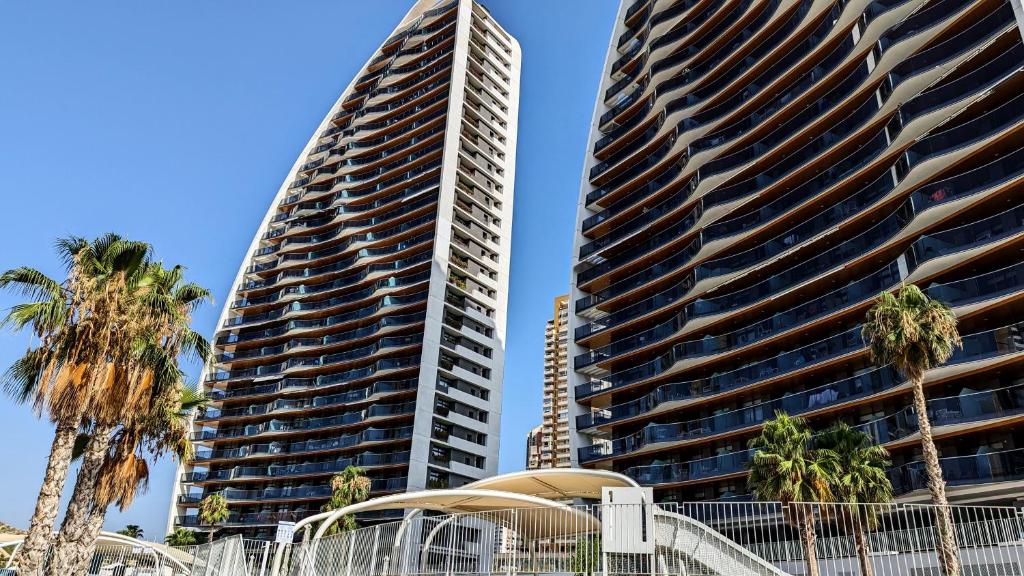 twee hoge gebouwen met palmbomen voor hen bij SUNSET WAVES sea & sky apartment in Benidorm