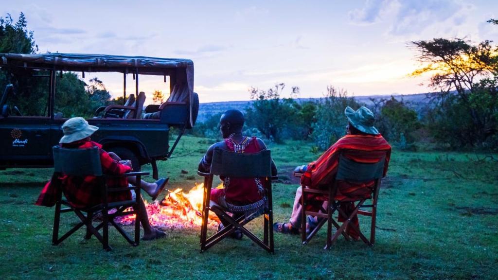 un grupo de personas sentadas alrededor de un campamento de fuego en Maasai home village, en Sekenani