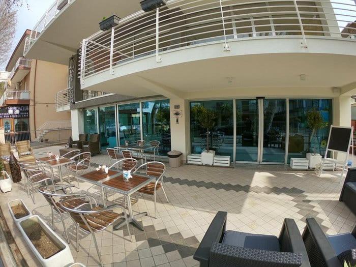 un patio avec des tables et des chaises en face d'un bâtiment dans l'établissement HOTEL HALF MOON RESTAURANT, à Rimini