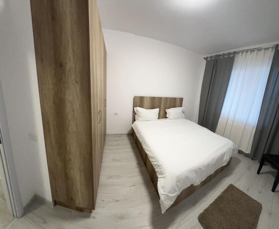 - une chambre avec un lit doté de draps blancs et d'une tête de lit en bois dans l'établissement Nova Residence Leordeni, à Popeşti-Leordeni