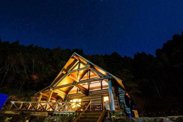 Yufuin Log House no Yado Tom Sawyer في يوفو: منزل مع سقف مضاء في الليل