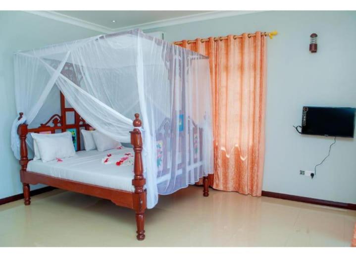 a bedroom with a canopy bed and a television at Taj hotel partnership in Nungwi