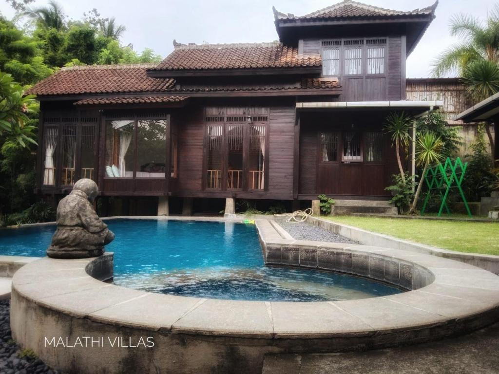 a pool in front of a house with a statue in front at Wooden House Pool View by Malathi Villas in Ubud