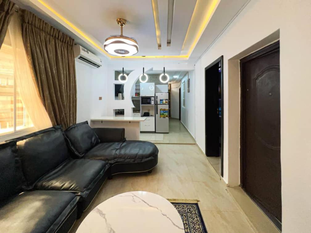 a living room with a black leather couch and a kitchen at Fey Pad in Lagos
