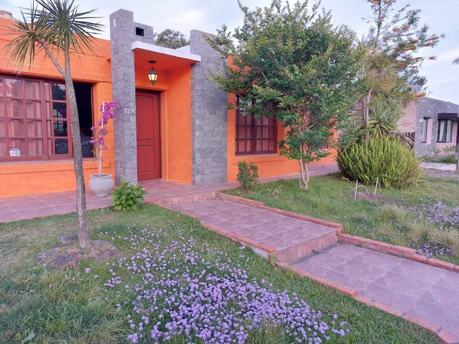 una casa arancione con fiori viola nel cortile di Roca de Guía. Casa con piscina y barbacoa cerca del mar a Punta del Este