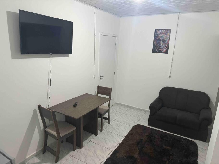 ein Wohnzimmer mit einem Tisch, einem Stuhl und einem Sofa in der Unterkunft Studio novo 2024 próx. Aeroporto in Passo Fundo
