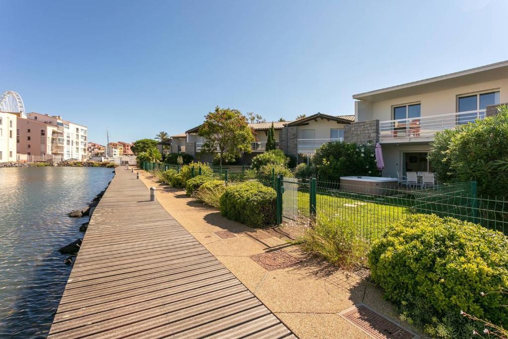 une passerelle en bois à côté d'une rivière avec des maisons dans l'établissement MARINA ILE ST MARTIN Joli 4 pièces avec jacuzzi Cap d'Agde, au Cap d'Agde