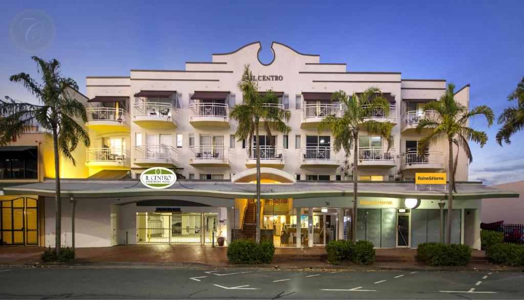 a white building with palm trees in front of it at Il Centro Apartment Hotel in Cairns