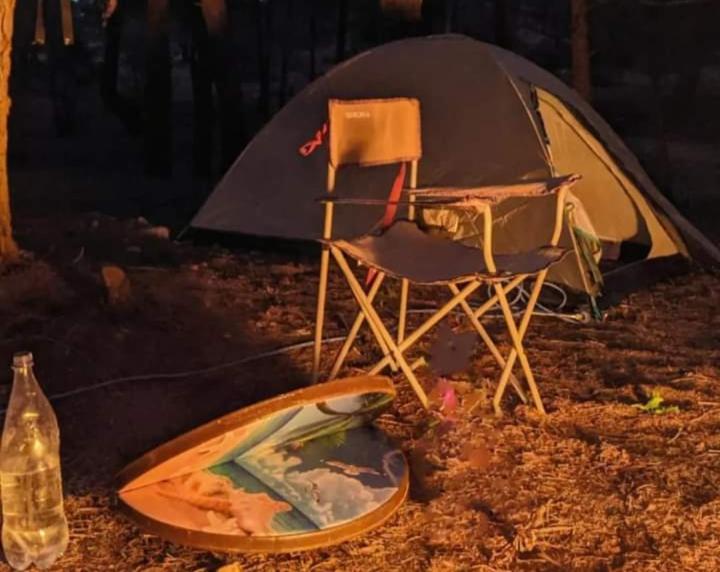 a tent and a chair and a surfboard on the ground at Orion's wild camp in Dana