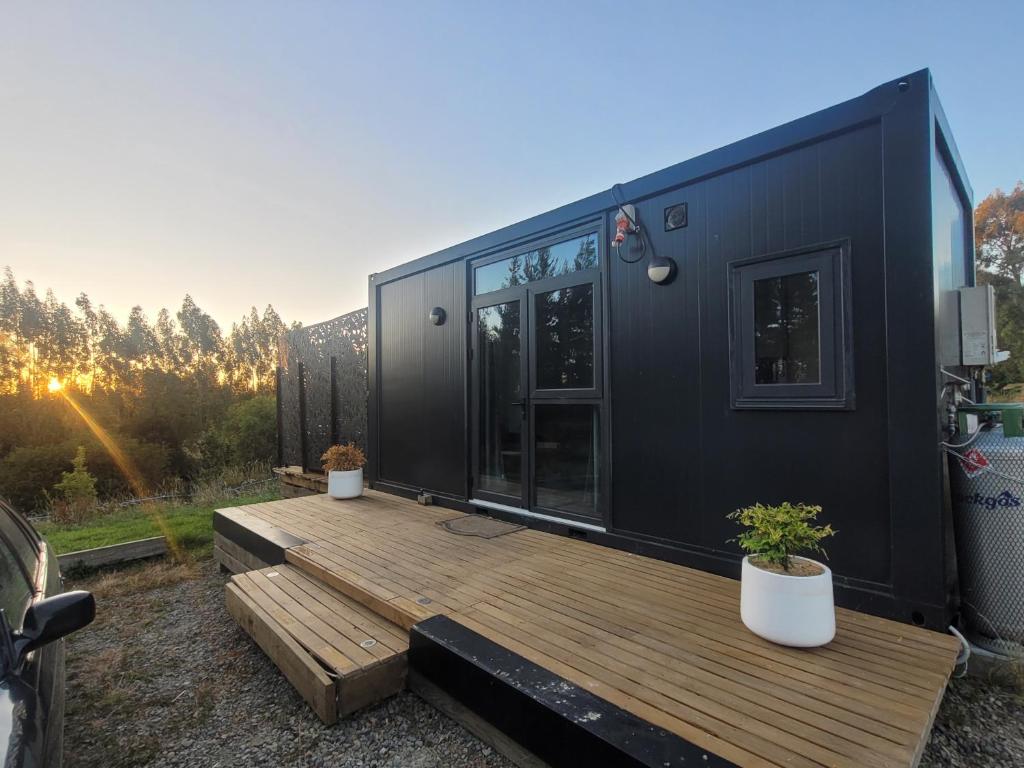 Hilltop Rural Retreat في Loburn: منزل صغير أسود مع شرفة خشبية