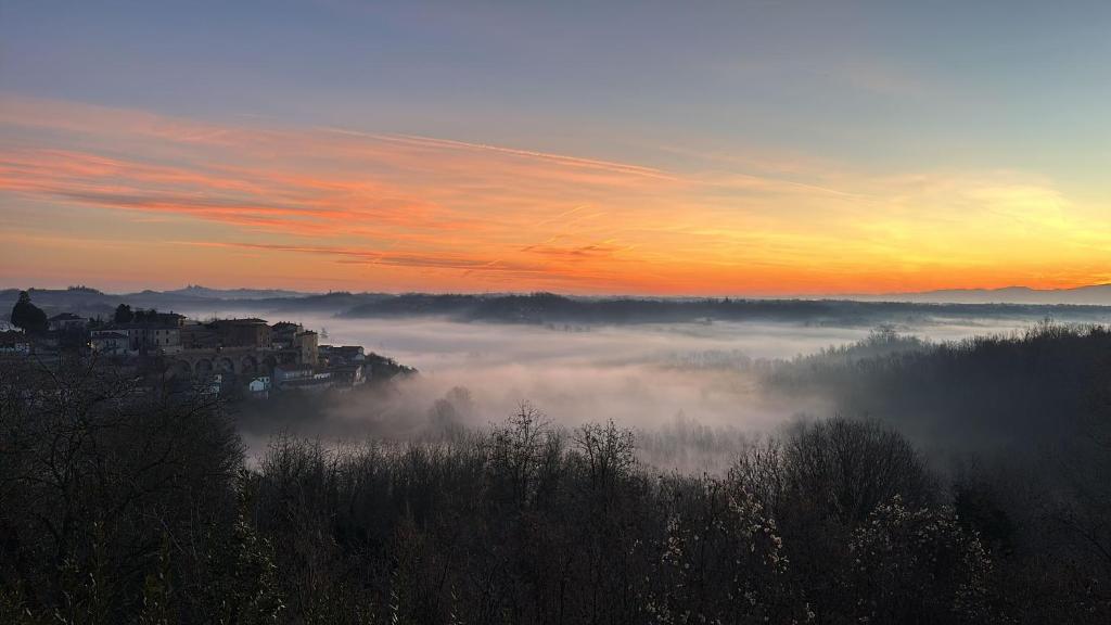 a foggy field with a city in the background with the sun setting at Vita Bella in Castagnole Monferrato