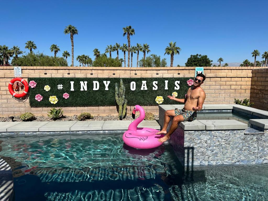 a man sitting next to a pink swan in a swimming pool at IndyOasis: pool*spa*games*BBQ*4BR2BA. Wlk2Festivls in Indio